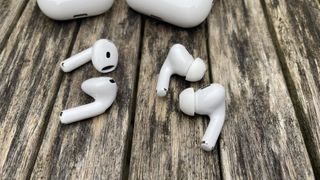 The Apple AirPods 4 and AirPods Pro 2 earbuds lying next to each other on a wooden surface.