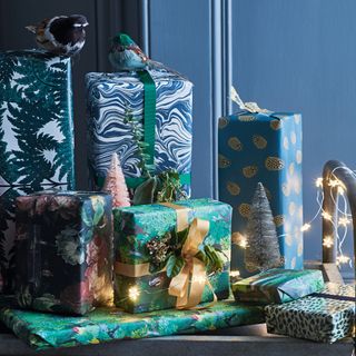 Christmas presents wrapped in blue and green patterned paper with lights and a bird ornament