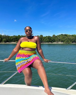 Woman on a boat wearing a yellow bikini and colorful crochet skirt.