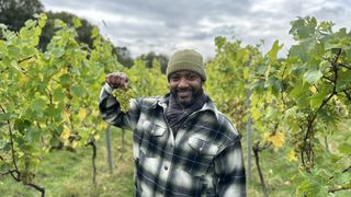 JB Gill stands in a vineyard holding grapes in Winter on the Farm.