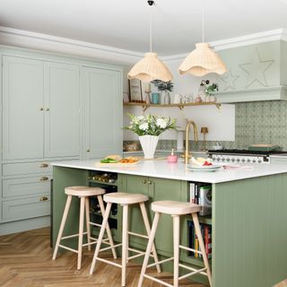 green kitchen island underneath woven pendant lights, next to floor to ceiling storage units