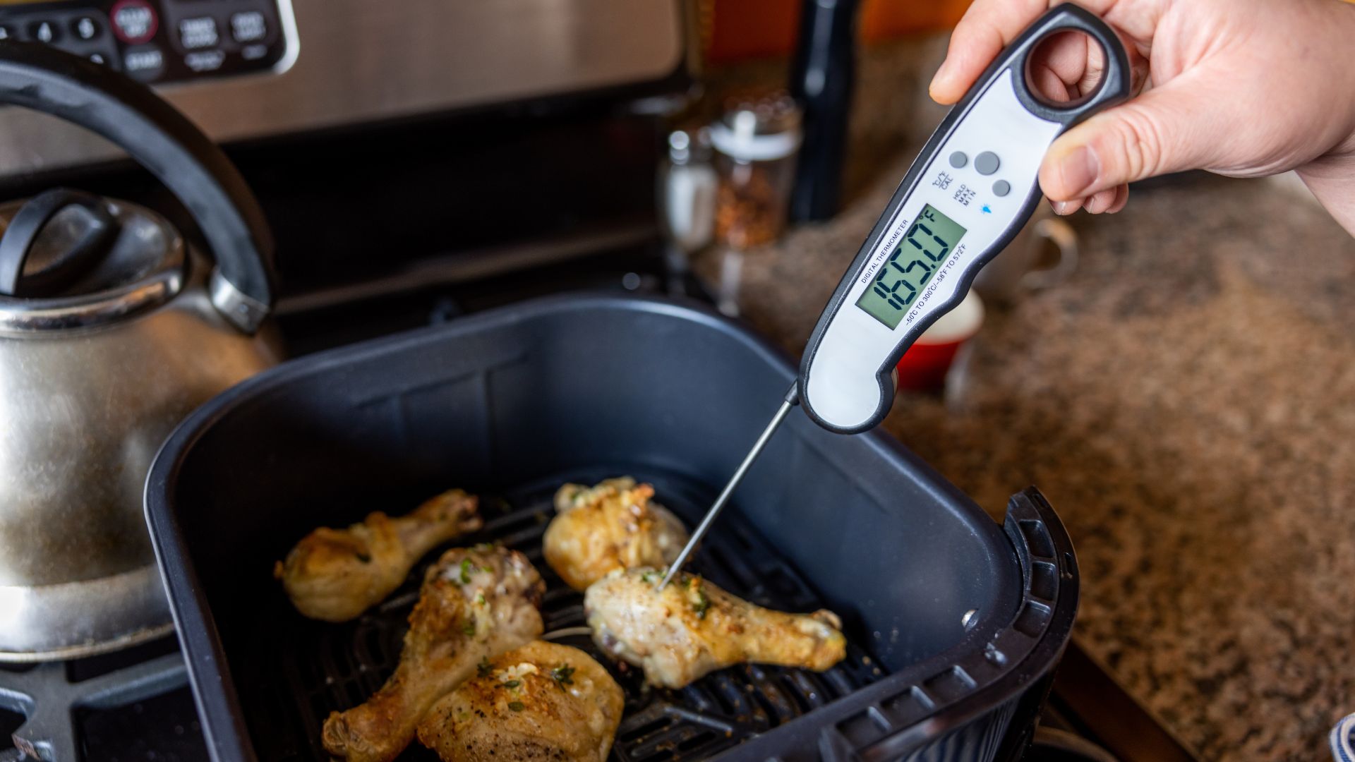 Person checking the internal temperature of chicken drumsticks using a temperature probe