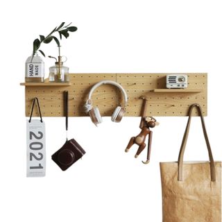 A vertical wooden pegboard with a bag, plant, and headphones on it