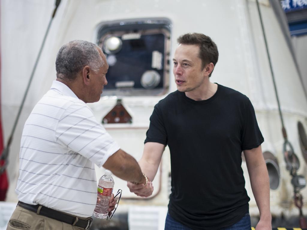 Charlie Bolden and Elon Musk shake hands by SpaceX&#039;s Dragon capsule