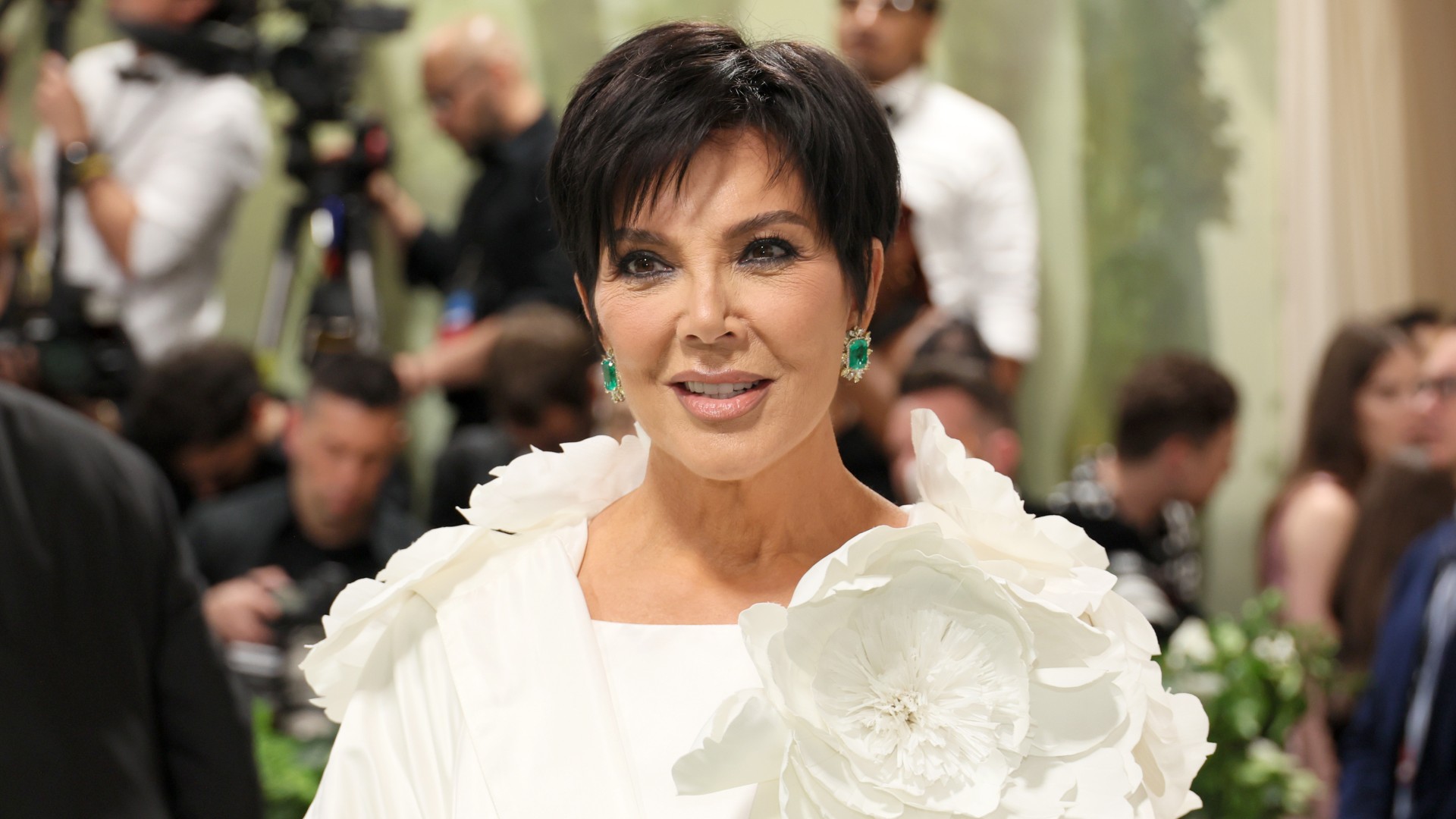 a paparazzi photo of a white woman with short, black hair wearing a white gown with a flower attachment