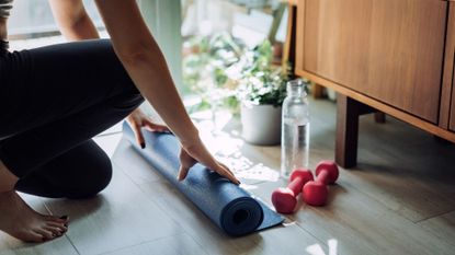 Person unrolls exercise mat beside a full water bottle and dumbells