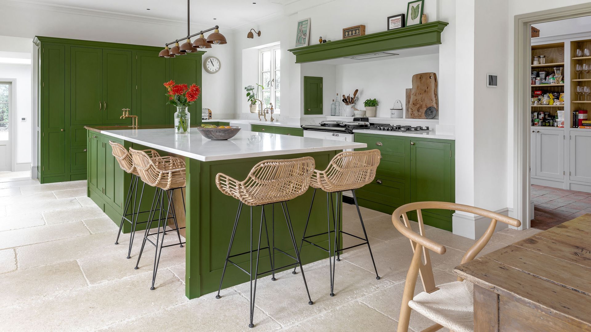 A white and green kitchen with Shaker-style cabinetry, kitchen island, rattan bar stools and white countertops.