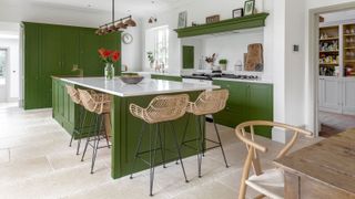 A white and green kitchen with Shaker-style cabinetry, kitchen island, rattan bar stools and white countertops.