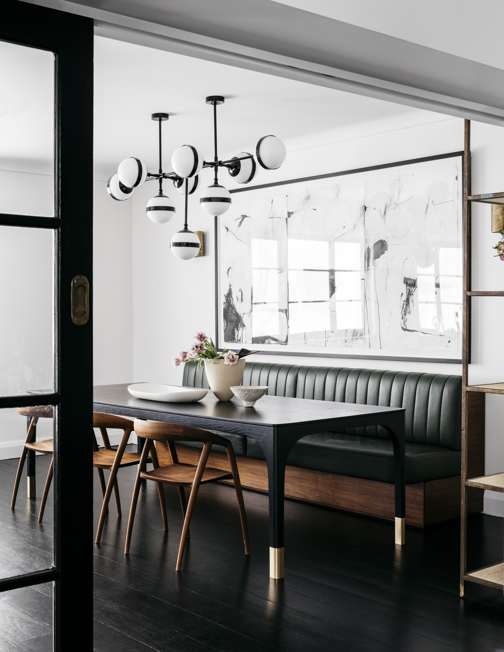 mid-century modern inspired dining room with banquette seat and timber chairs, large artwork, glass internal doors, dark floorboards, and mid-century inspired pendant light overhead