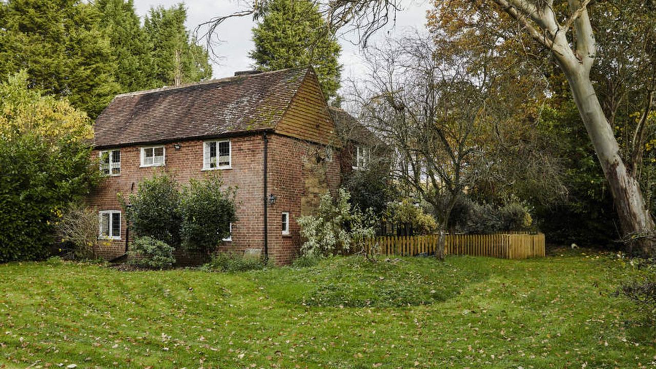 A traditional brown-brick home surrounded by a large lawn covered in autumn leaves