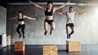 Three people jumping on to boxes next to eachother with a grey backdrop. 
