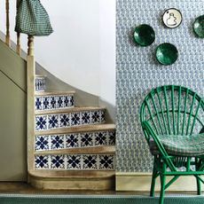 Hallway, wooden staircase with Mediterranean tile wallpaper pattern on risers, green wicker chair, green wall mounted ceramic plates. Floral printed wallpaper and floor carpet runner