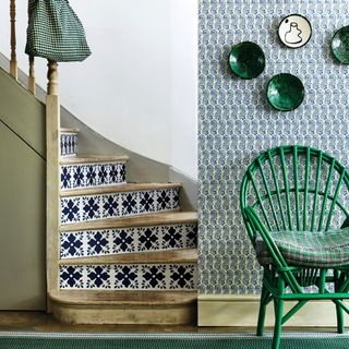 Hallway, wooden staircase with Mediterranean tile wallpaper pattern on risers, green wicker chair, green wall mounted ceramic plates. Floral printed wallpaper and floor carpet runner