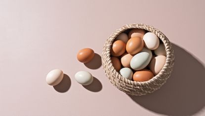 Three eggs sitting outside a basket of eggs.