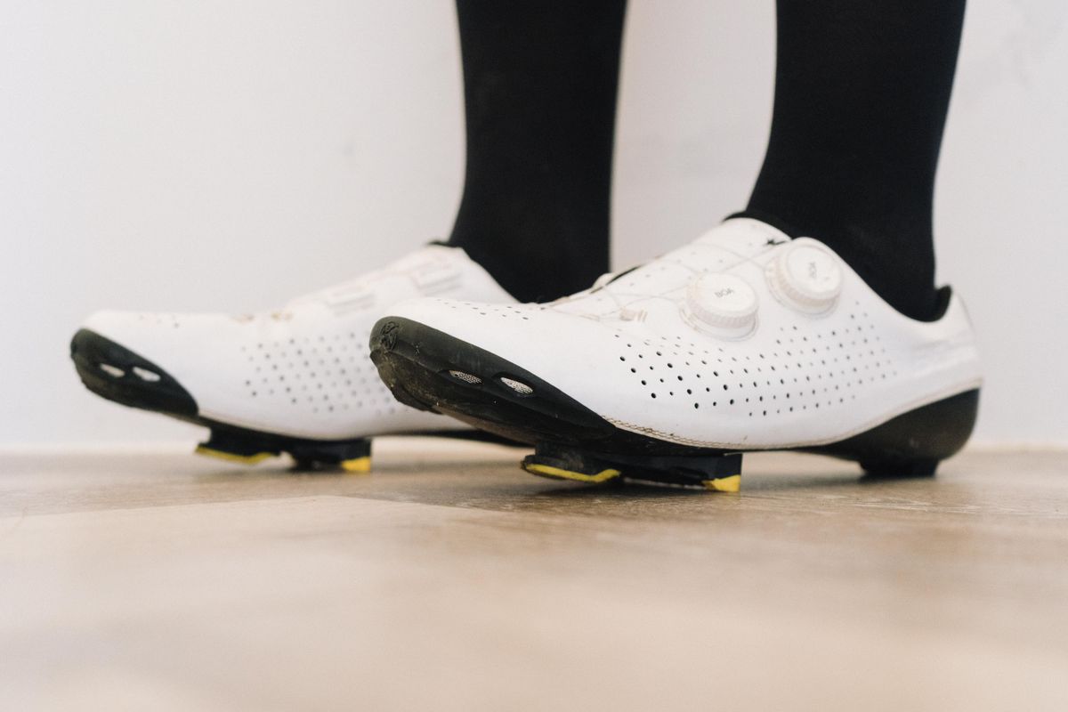 A close up of a white cycling shoe with a black socked foot in it