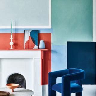 room with blue armchair, white fireplace, white table and multicoloured wall mural