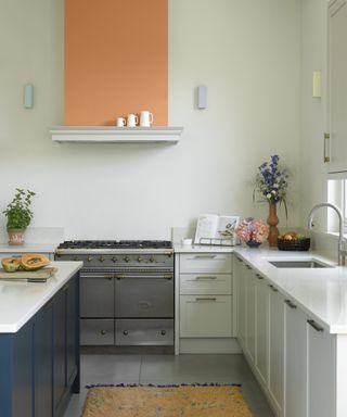 Blue and white kitchen with blue kitchen island, orange color block painted above cooker hood