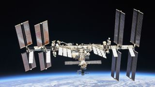 the international space station at a distance with solar panels shining against black space. earth is below