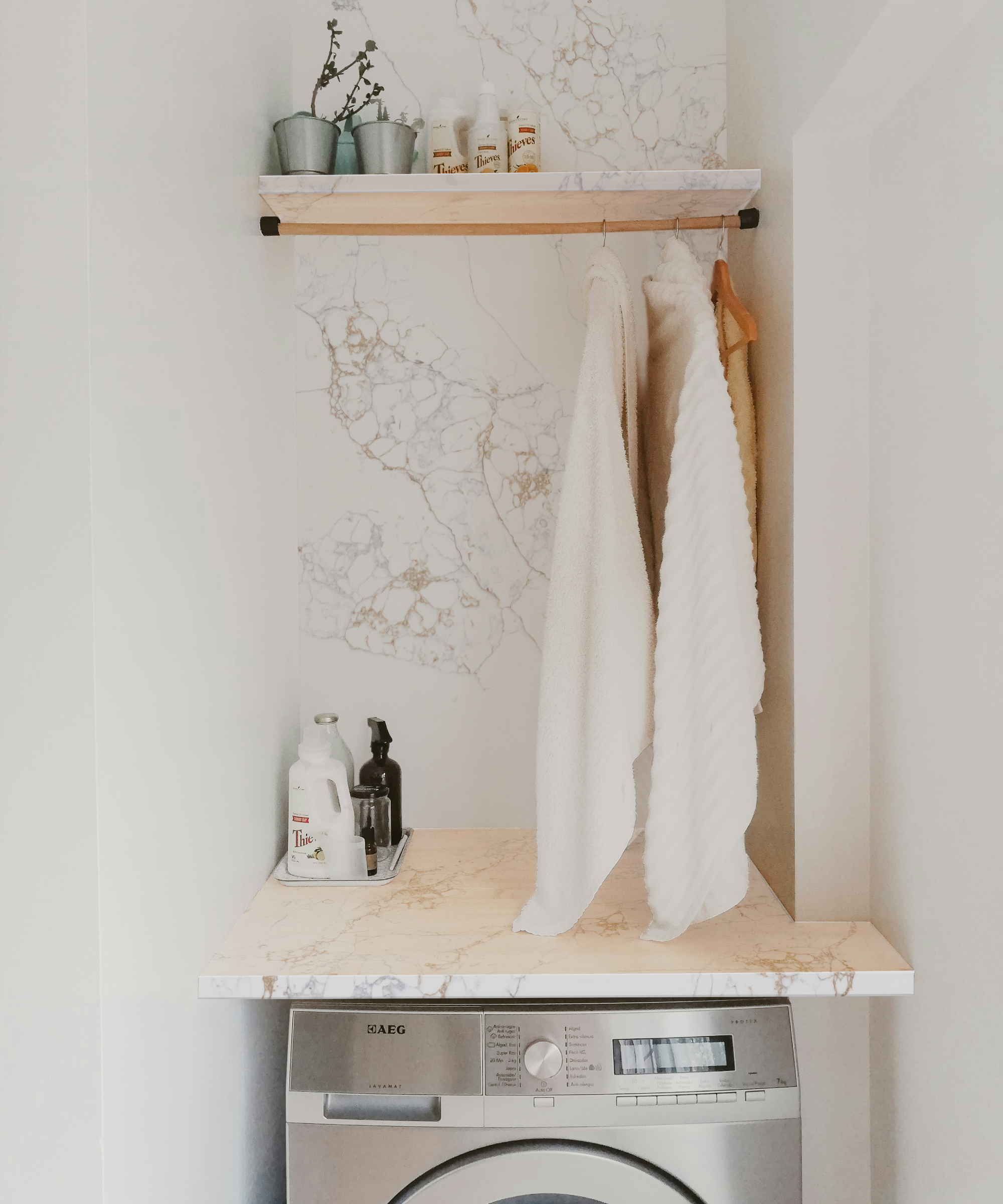 corner of utility room with washing machine and light coloured quartz worktop, back panel and shelf with hanging rail below