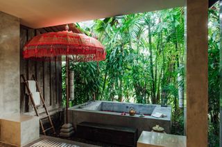 Red olivia parasol from east london parasol company near outdoor bath in tropical garden