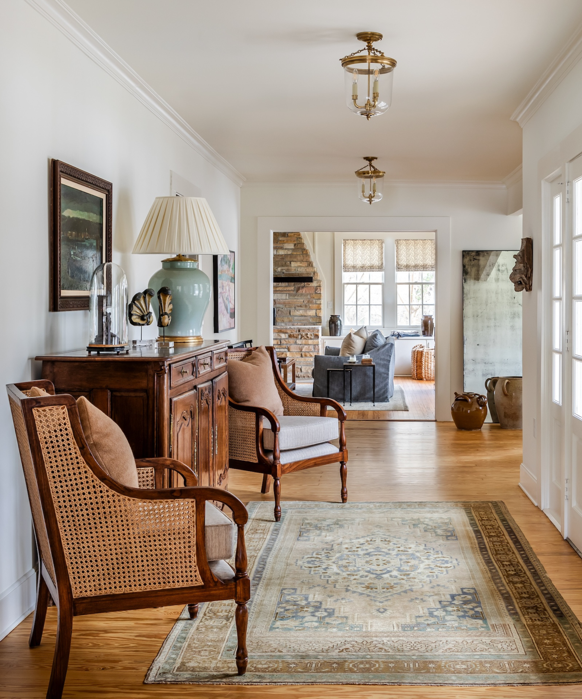 an entryway seating area with a persian rug on the floor, a large wooden sideboard, and two matching chairs with caning