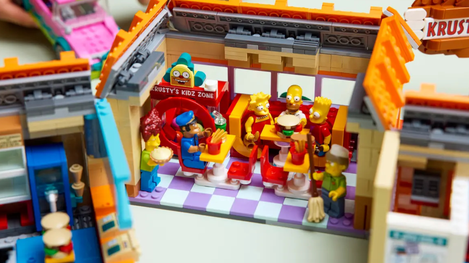 Lego Krusty Burger set on a plain surface, with a close-up of the minifigures seated inside