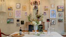 High-ceilinged dining room featuring ample wall art, with two of those works, which flank either side of the ornate fireplace and mantle mirror, being candle sconces in disguise.