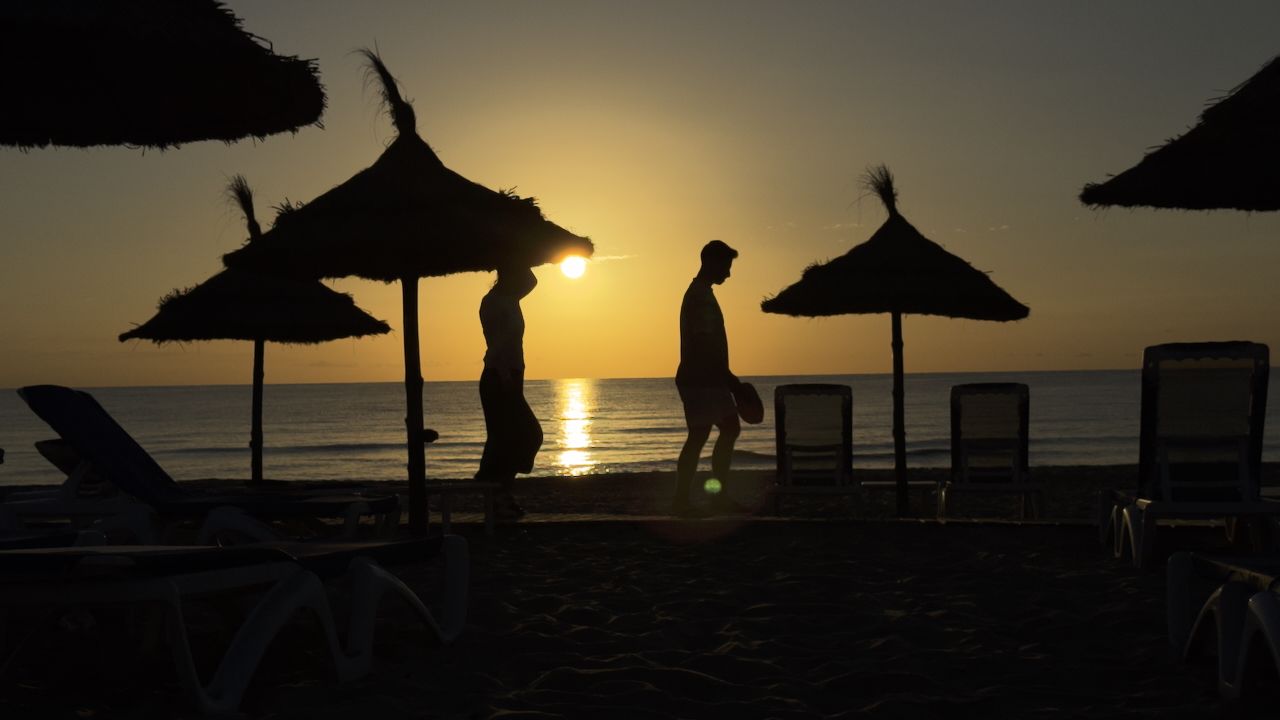 Two people silhouetted walking along a beach between parasols at sunset