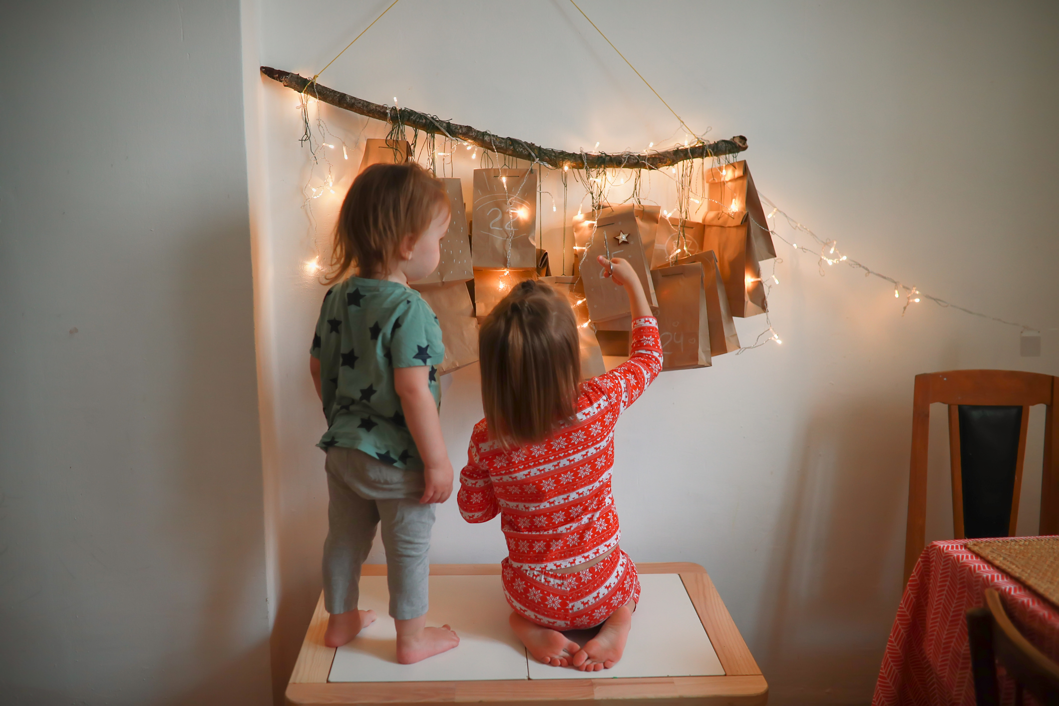 Brother and sister together are looking for package with gift on Advent calendar. Two kids in Christmas pajamas cuts off opens package with advent calendar.