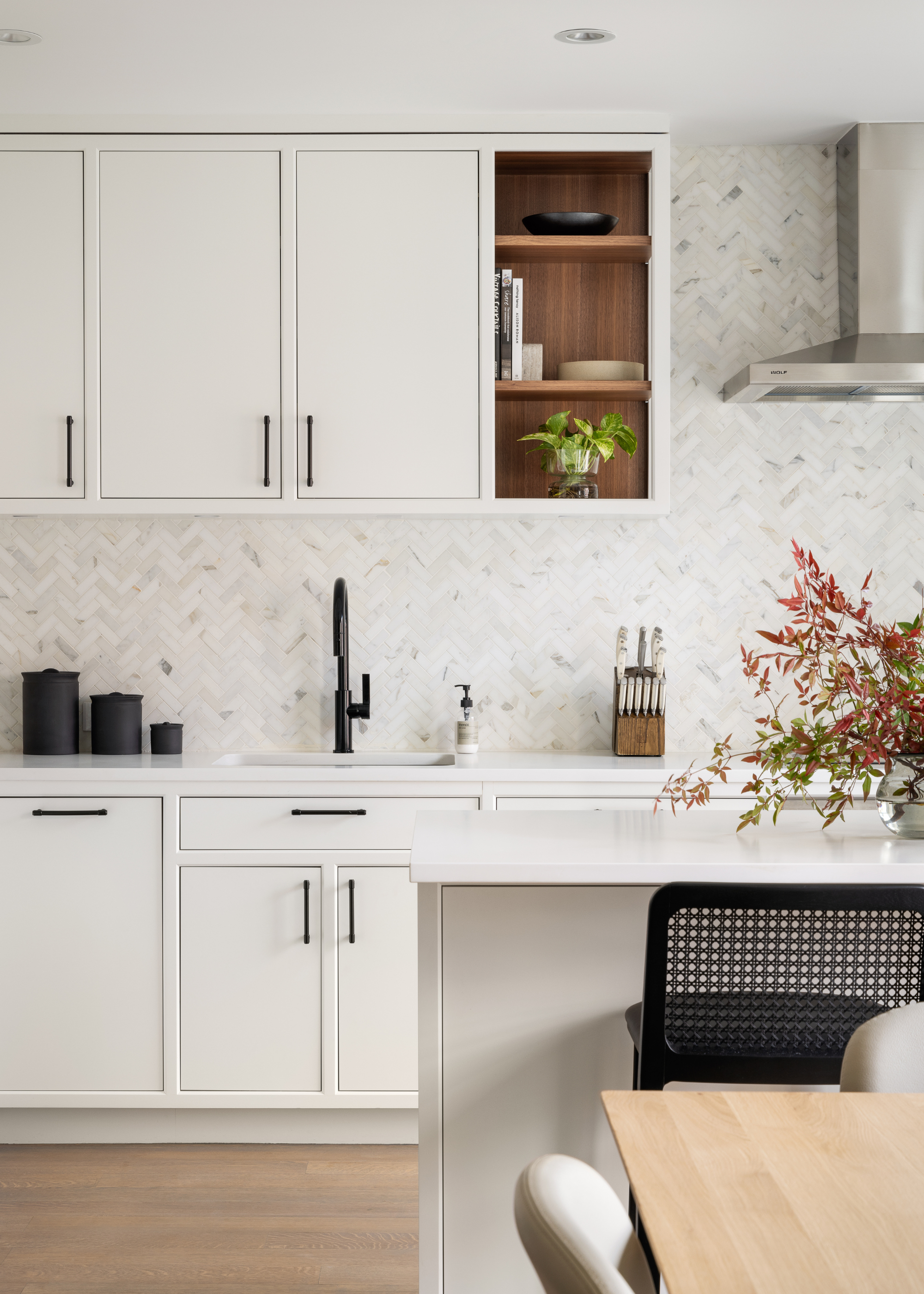 A white kitchen with a trio of black canisters, a knife block and a vase of stems