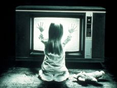 Girl sitting in front of bright white screen television and putting hands against screen 