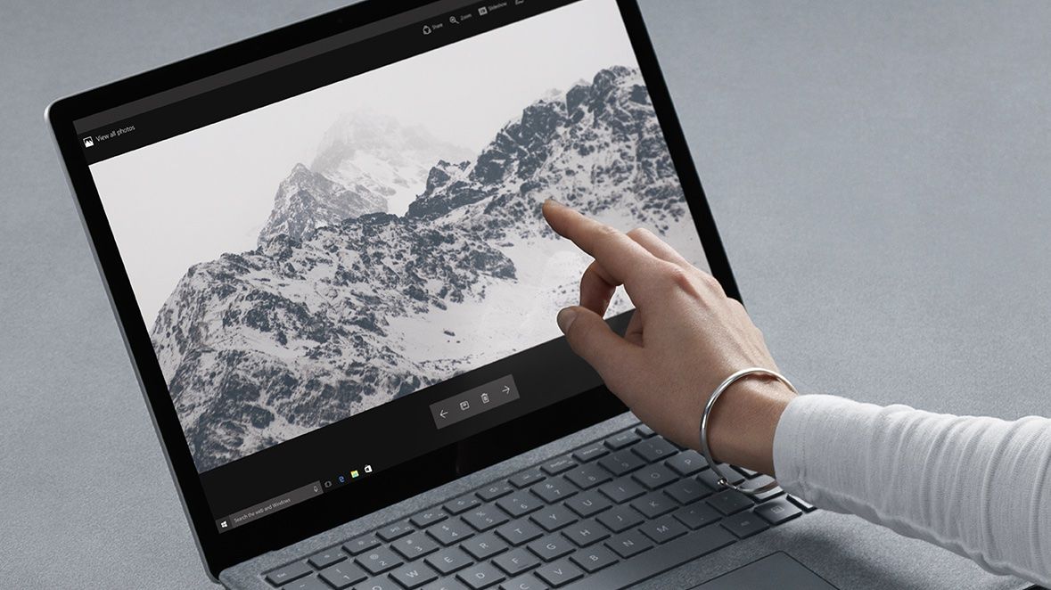 open laptop with desktop picture of snowy mountains, a lightskinned hand pointing to screen