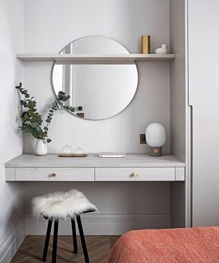 Dressing table in a grey alcove with circular wall mirror, fur topped stool, dark wooden flooring.