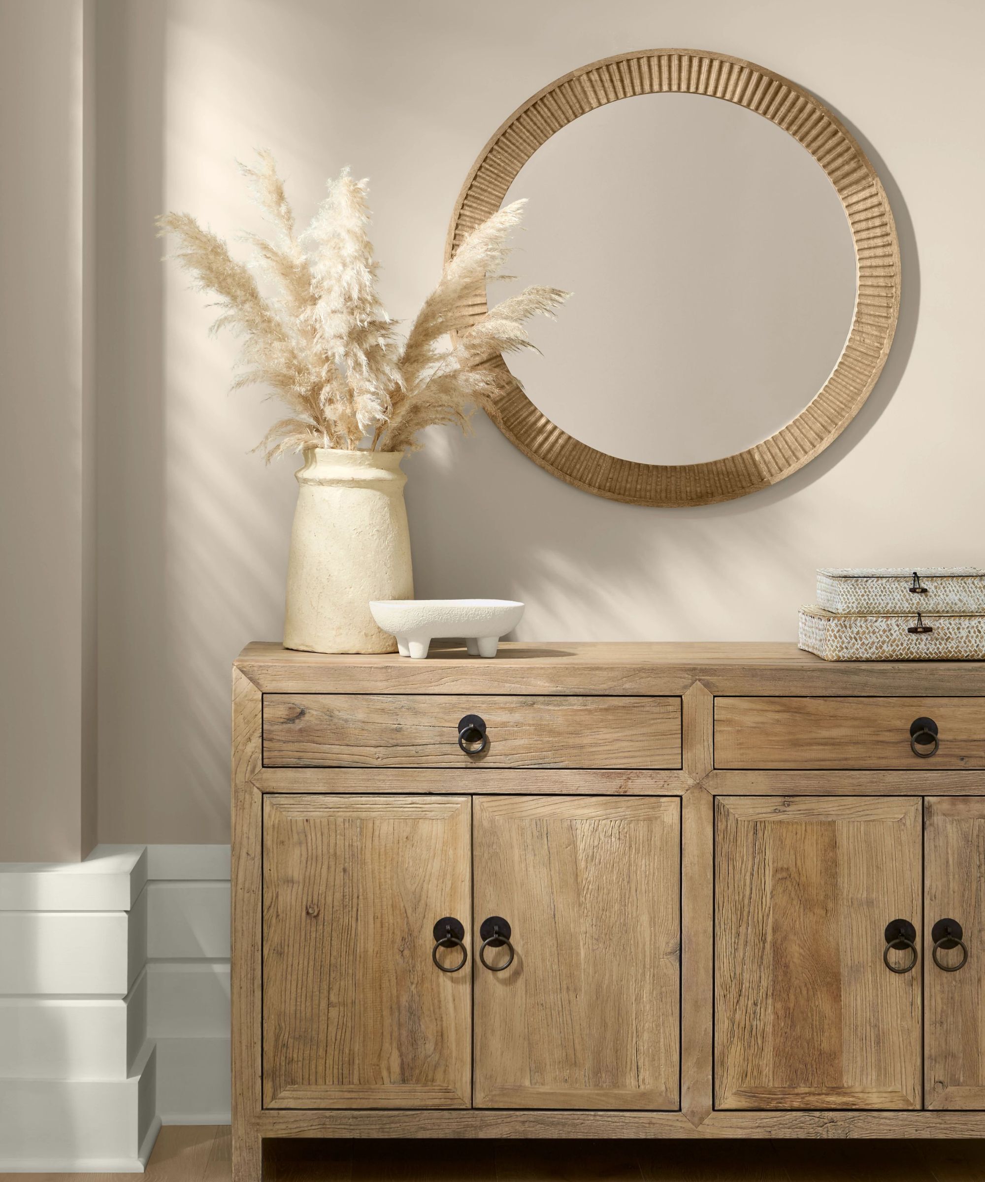 A pale wood cabinet with a circular mirror above, both against a wall painted in Shiitake by Sherwin Williams