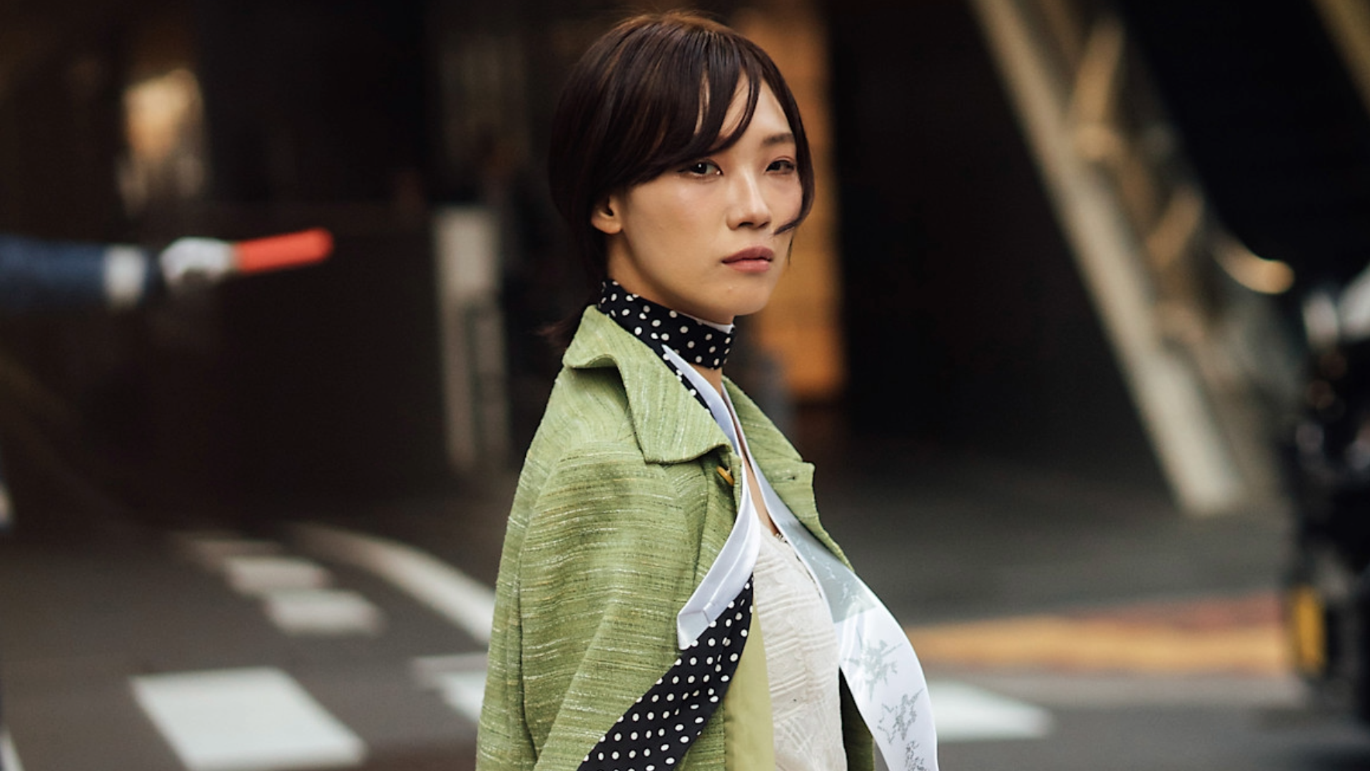 woman wearing a green jacket, polka-dot scarf, and white shirt. 