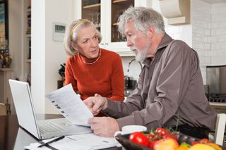 Senior couple looking concerned with bills and laptop - stock photo