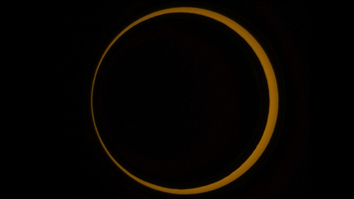 A picture of the moon's disk silhouetted by the outer edge of the sun, during an annular solar eclipse in a black sky.