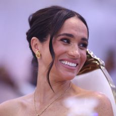 Meghan Markle attends an event with her hair up in a twist with gold earrings and a gold necklace
