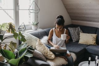 Young woman sitting on sofa with laptop, searching whether it's safe to book a holiday in 2021