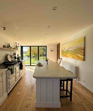 A traditional-style white in-frame kitchen with range-style cooker in a new extension. The kitchen features bifold doors to one end and a breakfast bar clad in tongue and groove cladding to the other. English ash barn grade flooring from Vastern Timber has been laid throughout.