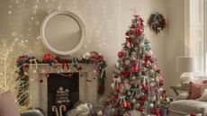 A living room decorated for Christmas with a tree and mantel garland featuring oversized baubles