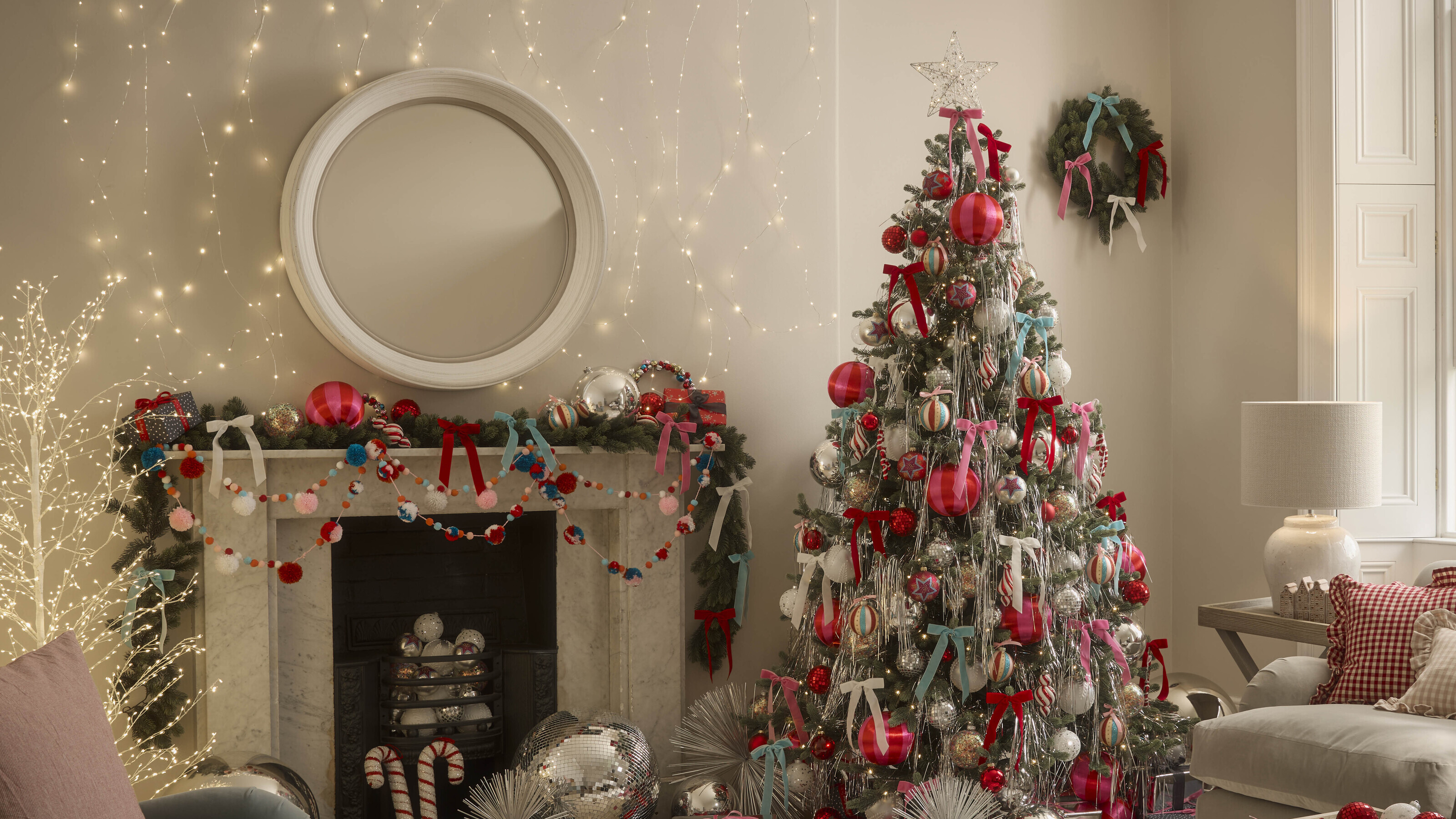 A living room decorated for Christmas with a tree and mantel garland featuring oversized baubles