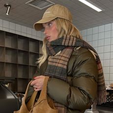 Elsa Hosk wearing a Polo Ralph Lauren baseball cap, olive green puffer jacket, plaid scarf, black pants, and boots