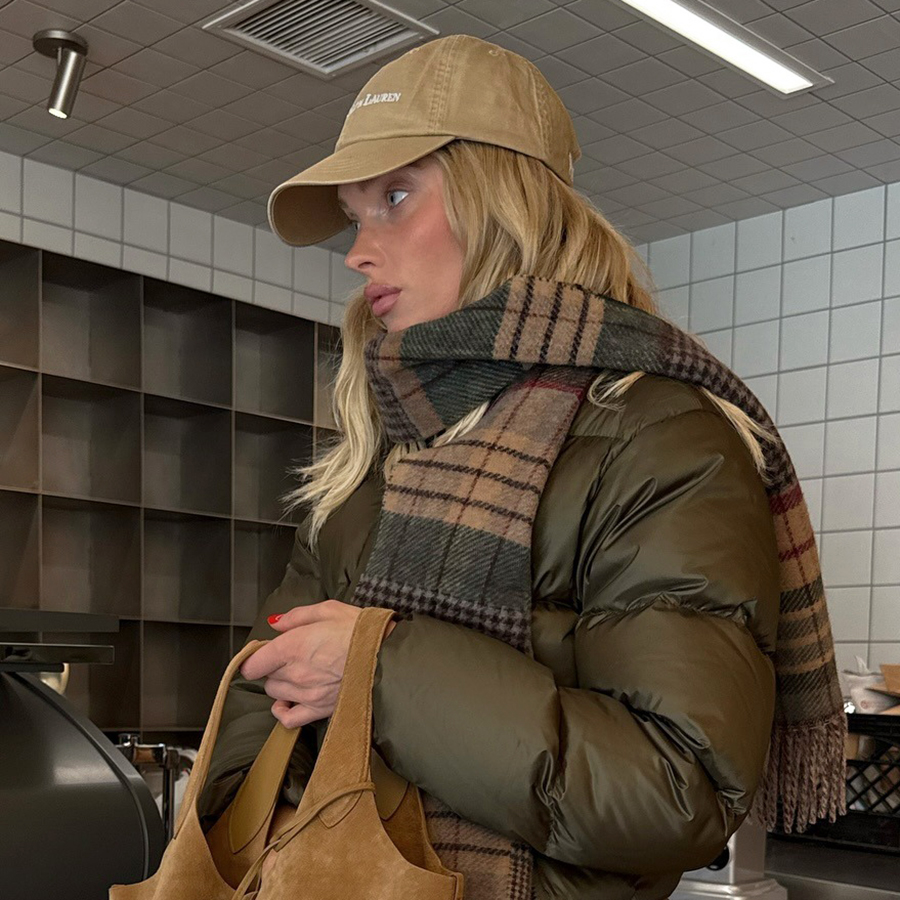 Elsa Hosk wearing a Polo Ralph Lauren baseball cap, olive green puffer jacket, plaid scarf, black pants, and boots