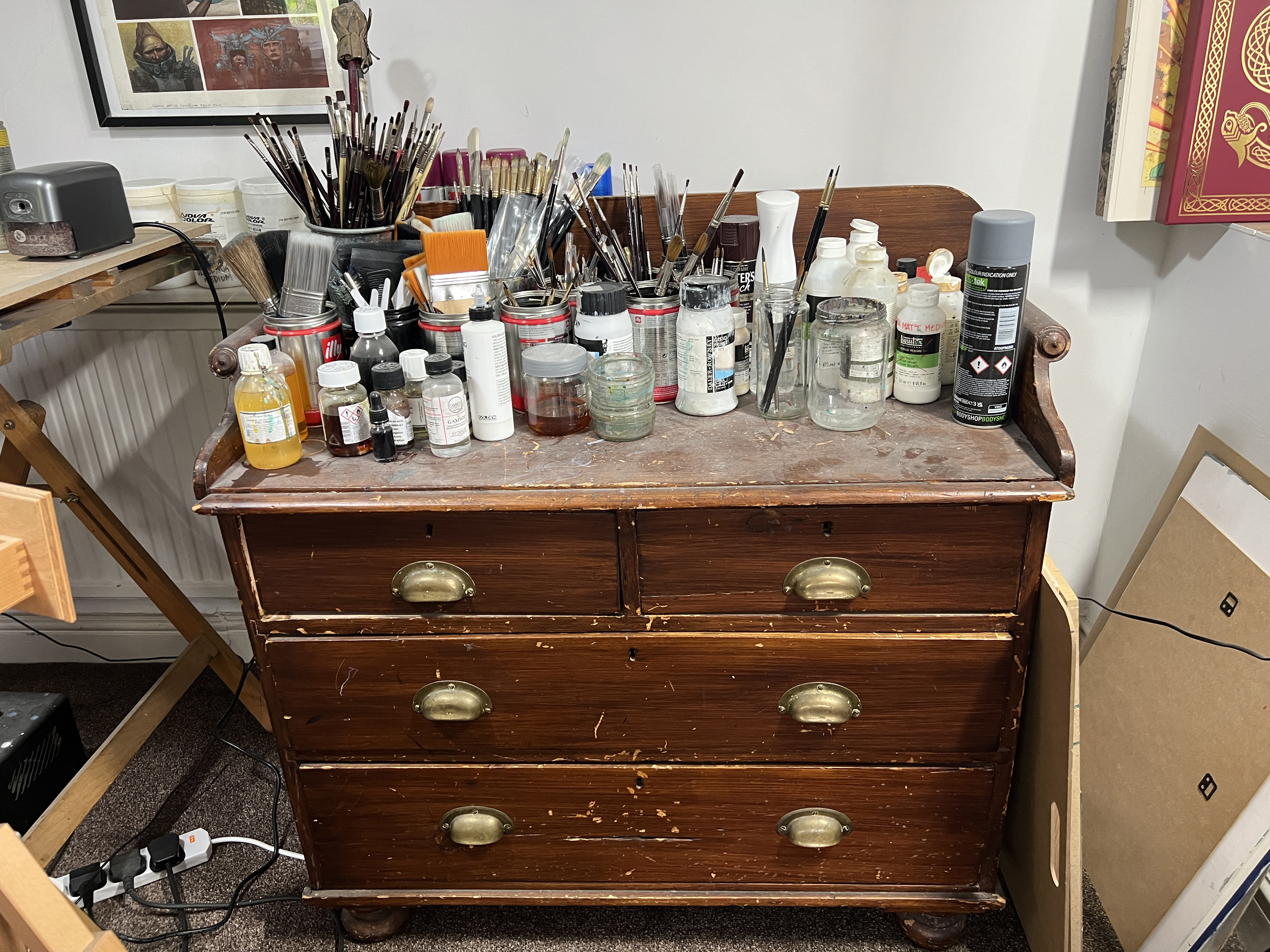 A chest of drawers topped with jars containing paint brushes in an artist's workshop