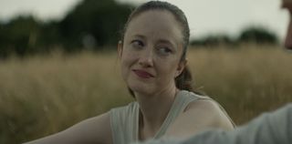 Andrea Riseborough in a light top sits in a field as Alice in Alice & Jack
