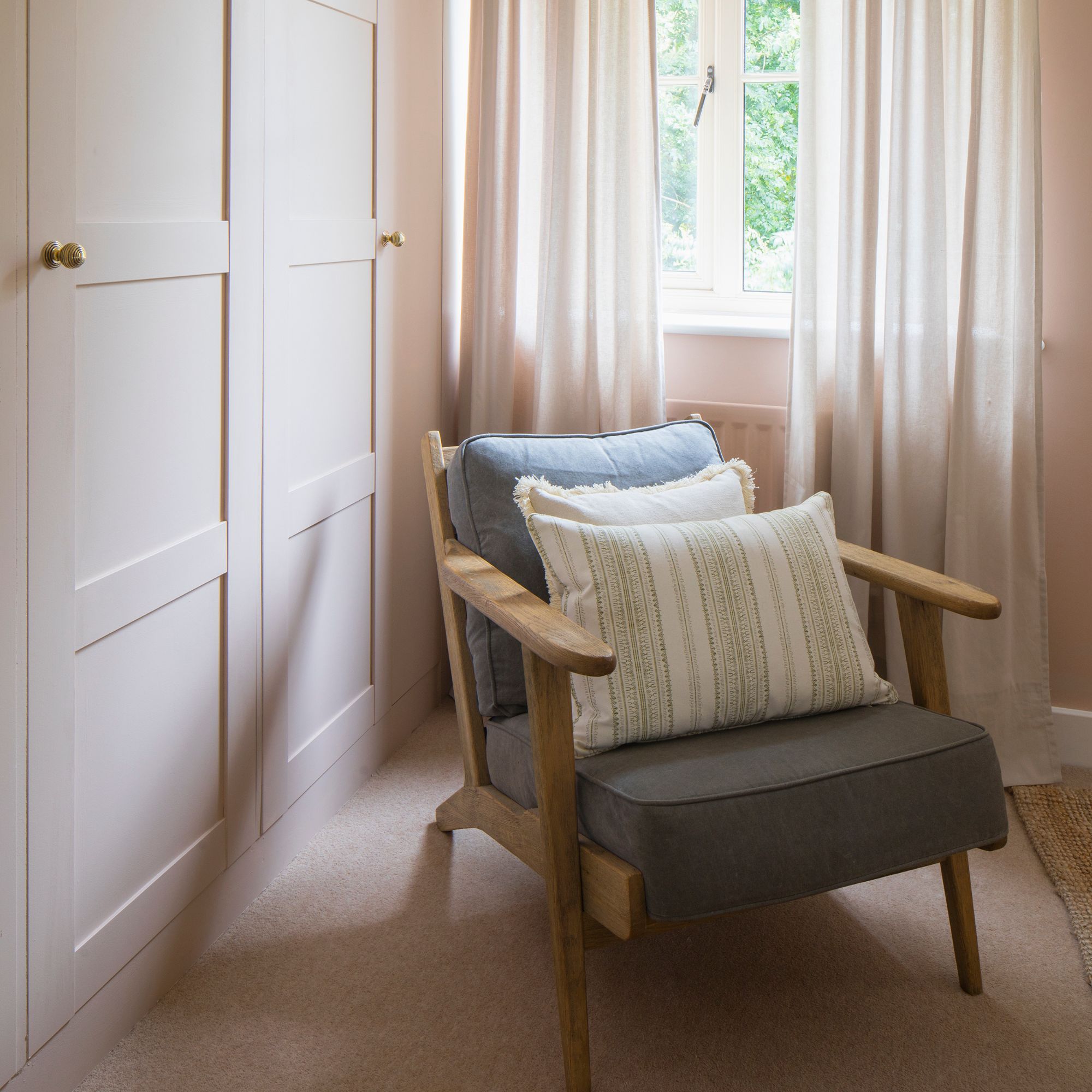 Light pink dressing room with fitted wardrobes to one side and a grey accent chair sitting in the middle