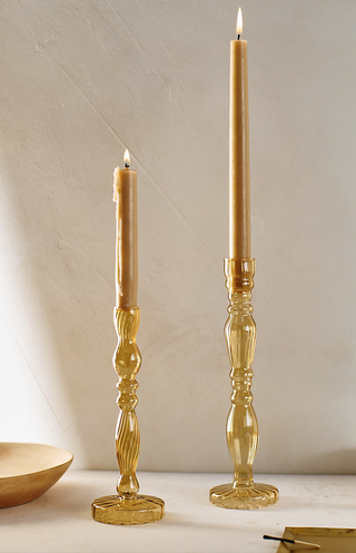 two glass candlesticks of different heights hold tapered candles on a tabletop