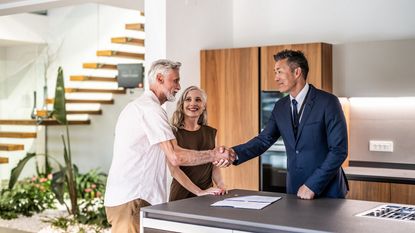 A senior couple shake hands with a realtor after negotiating when buying a home.