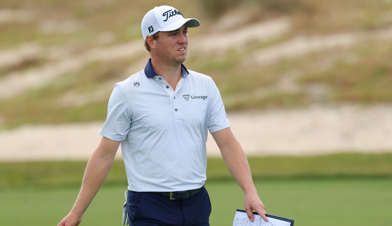 Justin Thomas walks down the fairway holding his yardage book